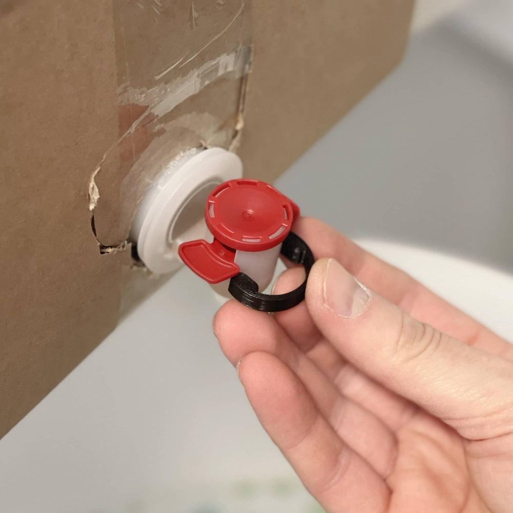 En hånd betjener Fresh Wort Kit Dispense Clip - Black Edition, som er festet til en bag-in-box for enkel væskedispensering.