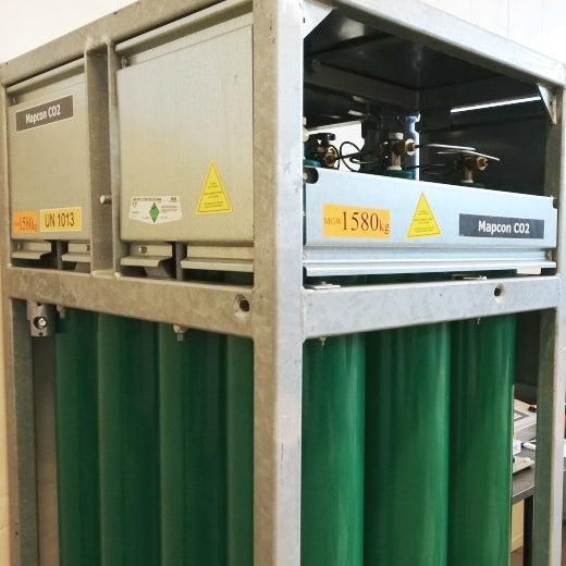 En oppbevaringsenhet i metall inneholder grønne Mapcon CO2-flasker med advarsels- og vektetiketter. Disse inneholder Brewshop Fylling av næringsmiddelgodkjent CO2 (Trondheim), egnet for næringsmiddelbruk og tilgjengelig for påfylling i Trondheim.