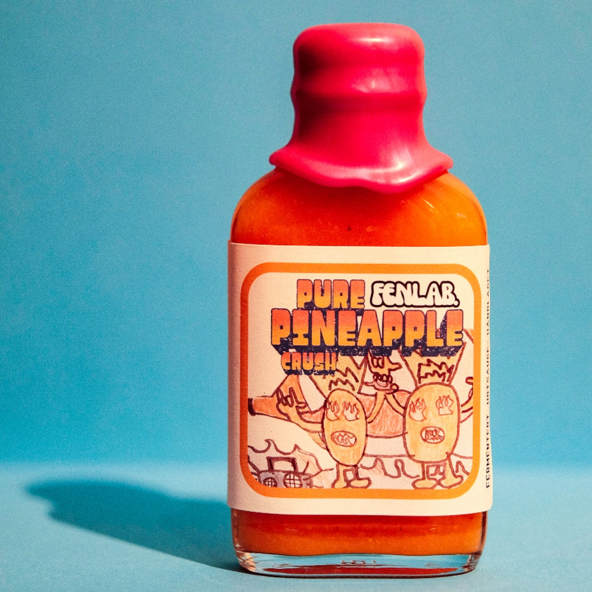 En flaske med varm saus med rosa voksforsegling og etiketten "Pure Pineapple Crush | Fen Lab", med karikerte ananas på blå bakgrunn.