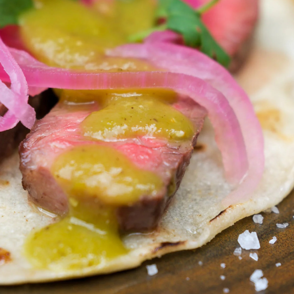 Nærbilde av en taco med biff i skiver, syltet rødløk, koriander, grovsalt og Kiwibber - Frisk Salsa Verde med Kiwi | Kyrres Krutt på en maistortilla.