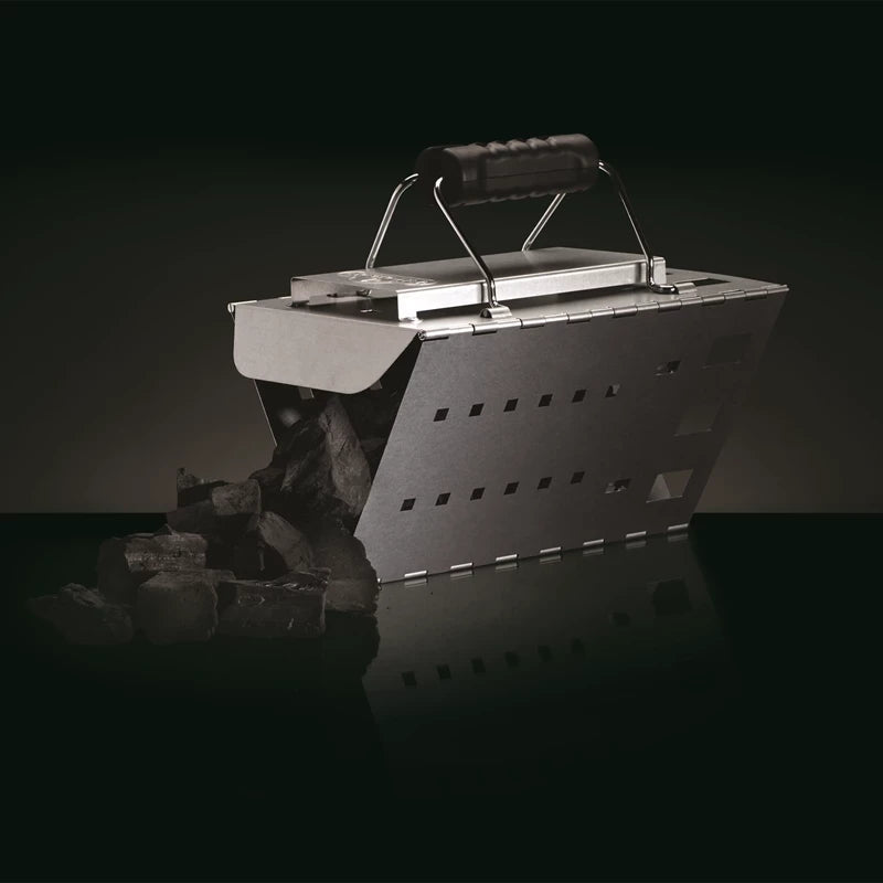 En Napoleon sammenleggbar grillstarter med svart håndtak, fylt med kullbriketter som renner ut på en svart flate - perfekt for enkel tenning av kullgrillen.