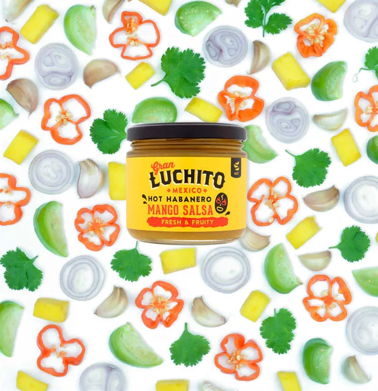 Et 330 ml glass med Gran Luchito Mango Salsa vises mot illustrert løk, paprika, agurk og ananas, noe som fremhever de livlige smakene i denne meksikanskinspirerte salsaen.