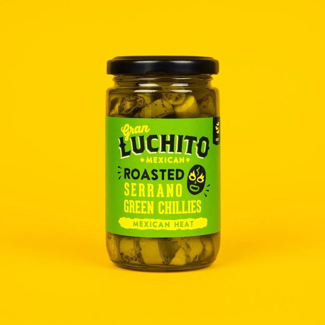 Et 215 g glass Gran Luchito Fire Roasted Serrano Chillies med grønn etikett skiller seg ut mot en gul bakgrunn - autentisk meksikansk serranochili med kraftig smak.