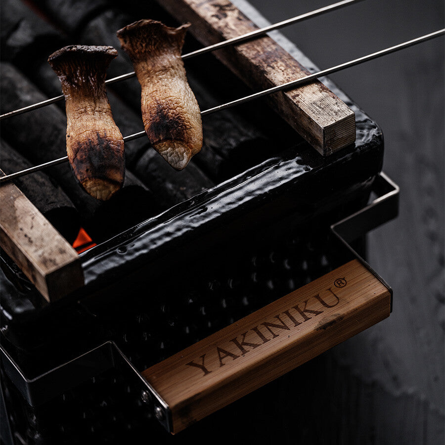 To sopper grilles på YAKINIKU BBQ Spyd i Rustfritt Stål 2,5 mm, hvert spyd hviler på en kullgrill merket YAKINIKU.