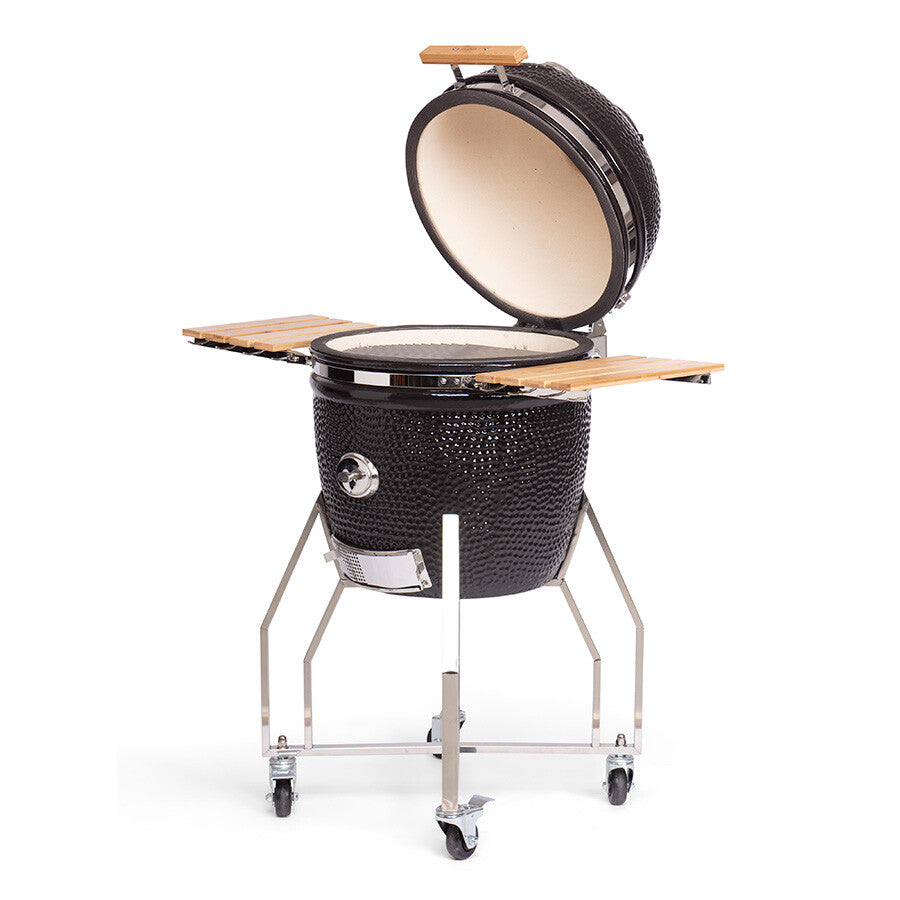 YAKINIKU Large Kamado Complete er en svart keramisk grill med åpent lokk, sidehyller i tre, en solid metallvogn og hjul. Den kombinerer klassisk design og moderne bekvemmelighet for alle dine utendørs matlagingsbehov.