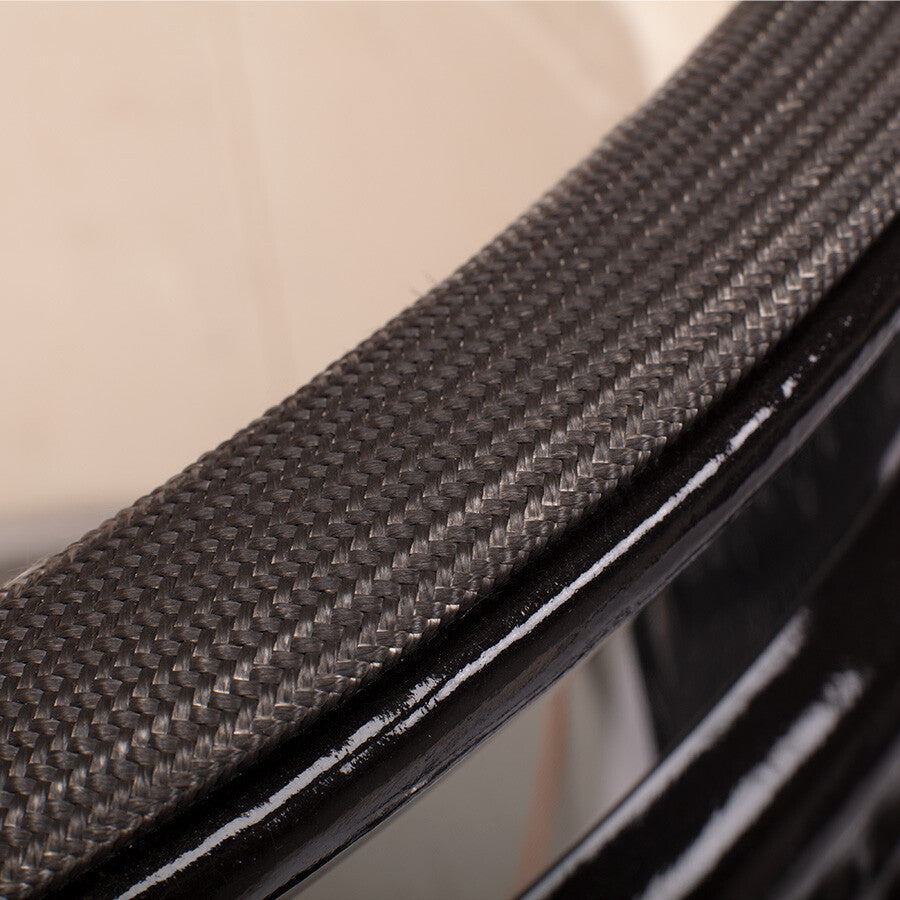 Nærbilde av en karbonfiberoverflate med vevd tekstur og blank, svart kant, som minner om den førsteklasses finishen på YAKINIKU Kamado XXLARGE Complete-grillen.