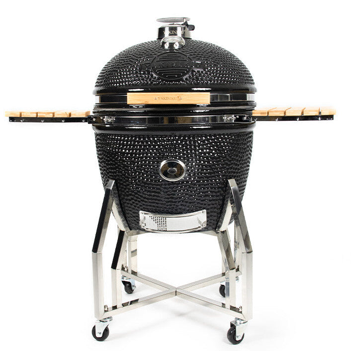 YAKINIKU Kamado XXLARGE 61 cm Complete er en svart keramisk grill med kuppelformet lokk, profesjonelle funksjoner, stativ i rustfritt stål, sidehyller i tre og hjul for enkel flytting, avbildet på en ensfarget hvit bakgrunn.