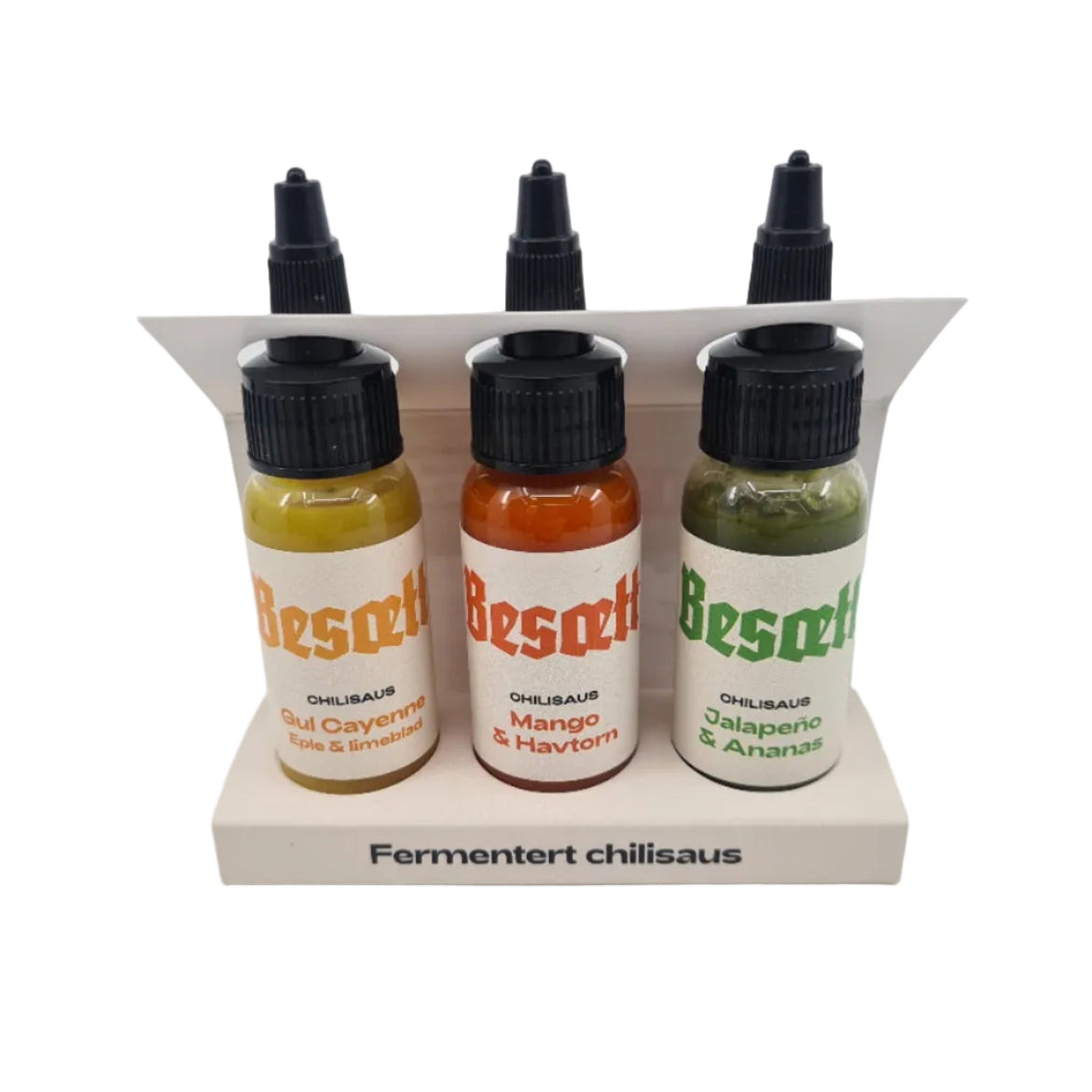 Tre flasker «Besætt Fermentert Chilisaus», hver på 33 ml og med forskjellige smaker, står oppreist i en hvit holder merket «Fermentert Chilisaus», og utgjør dermed den perfekte smakspakken for elskere av sterk saus.