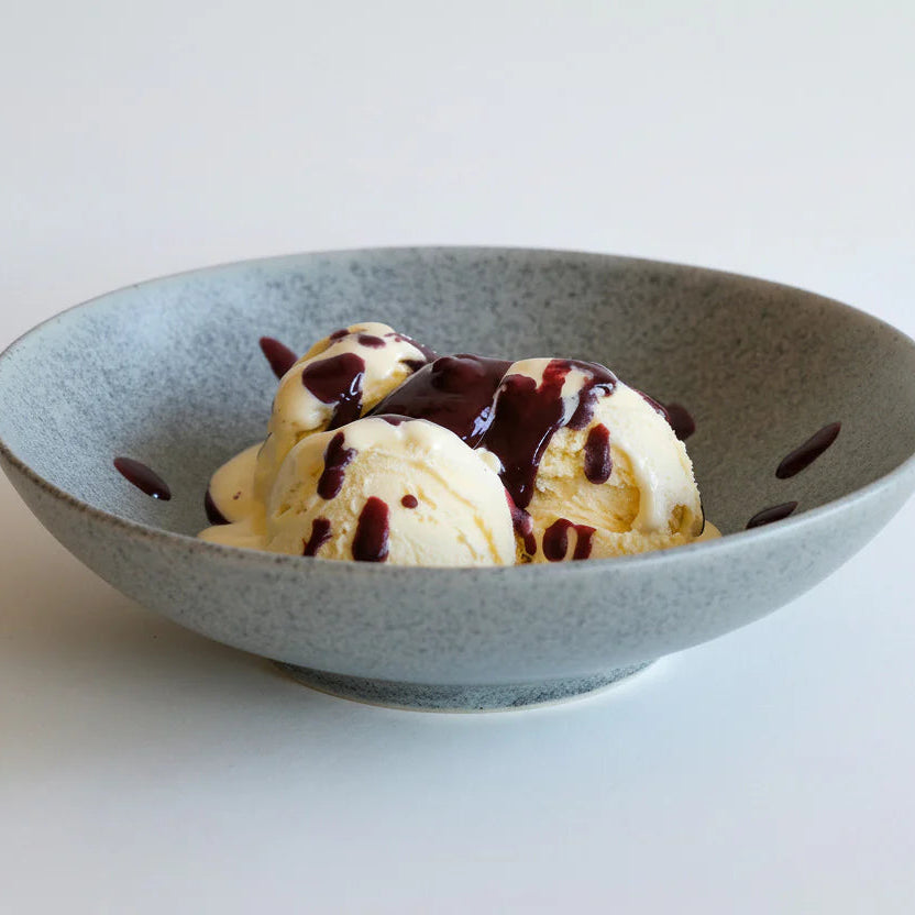 Tre kuler vaniljeis i en grå bolle toppet med Børnebær - Fruktig og søt chilisaus fra Kyrres Krutt, mot en enkel hvit bakgrunn.