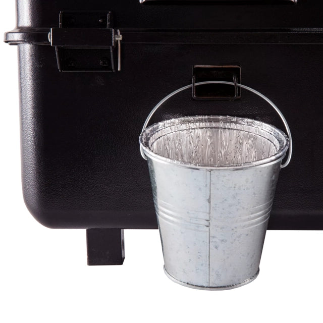 En Traeger Mini Bucket Liner 5-pakning – dryppbøtte er festet på siden av en svart grill, plassert under en åpning for å samle opp fett på en effektiv måte.