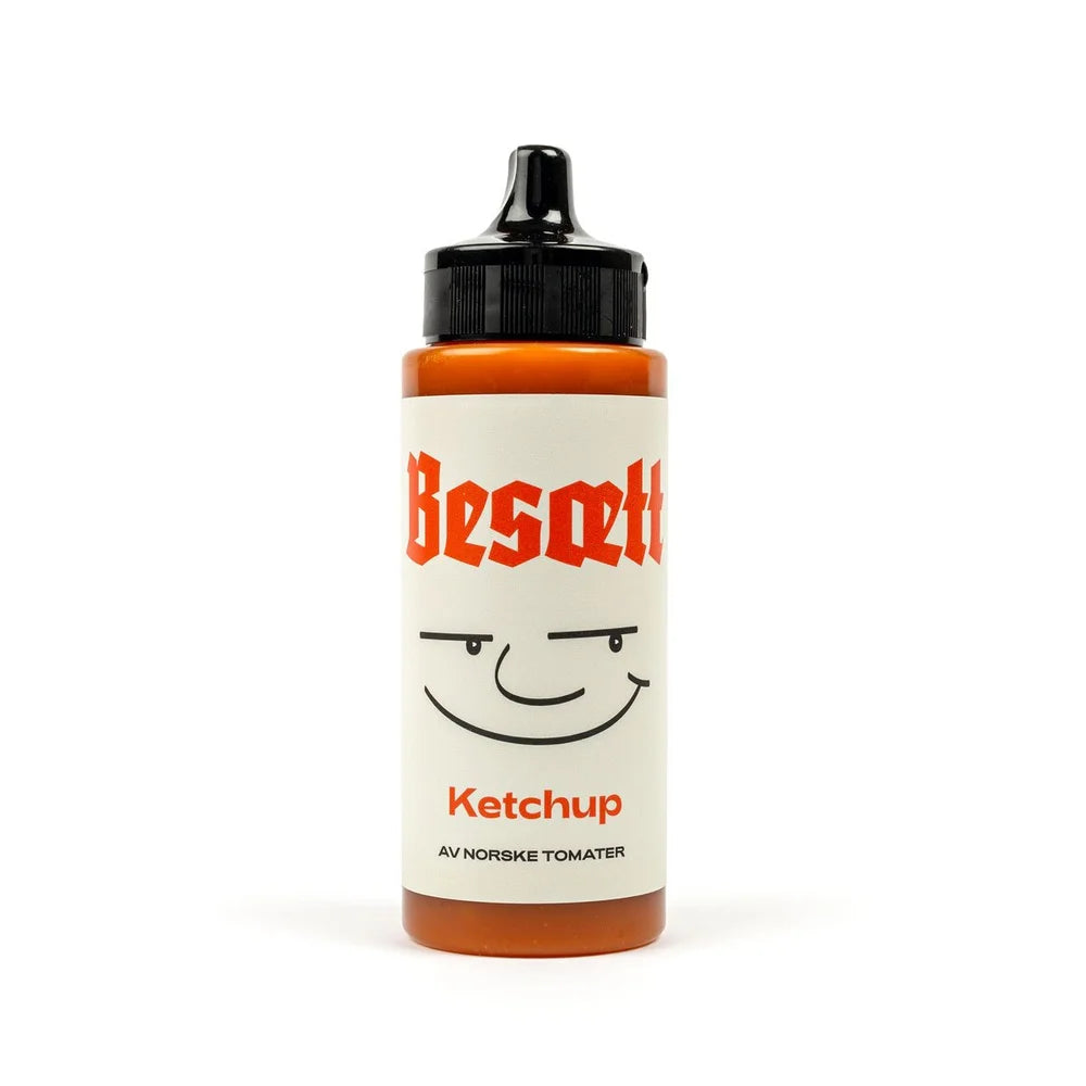 En flaske «Ketchup på Norske Tomater | Besætt» med et smilende ansikt på etiketten, som står oppreist mot en hvit bakgrunn.