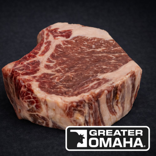 En rå, marmorert Storfe Entrecôte Greater Omaha-biff på 600 g på en mørk overflate med Greater Omaha-logoen nederst i høyre hjørne.
