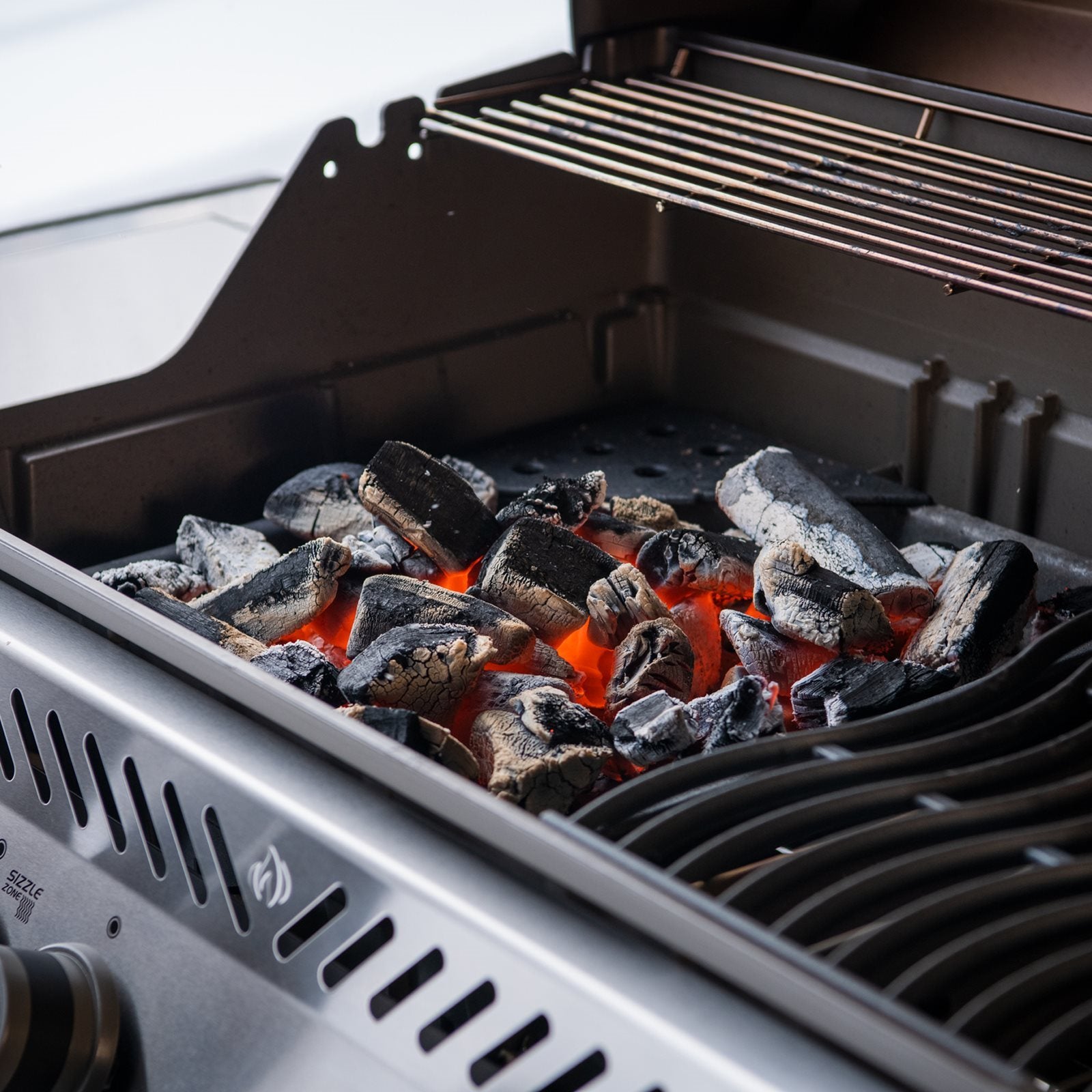 Nærbilde av en Napoleon Grillkullrist - kull- og røykebrett med glødende kullbriketter, rødglødende og dekket av hvit aske, klar til tilberedning på grillen din.