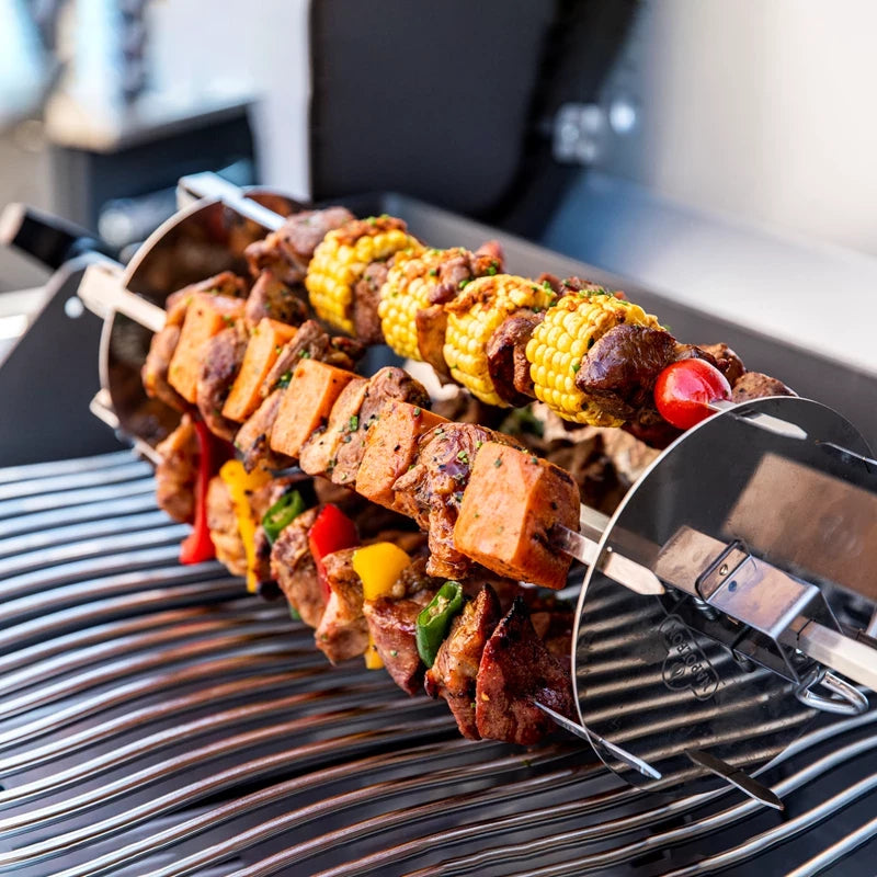 Flere spyd med kjøtt, grønnsaker og mais grilles på et metallspyd inne i en grill, ved hjelp av Napoleon Shish kebab-hjulet, som sørger for perfekt tilberedte og fargerike kebaber.