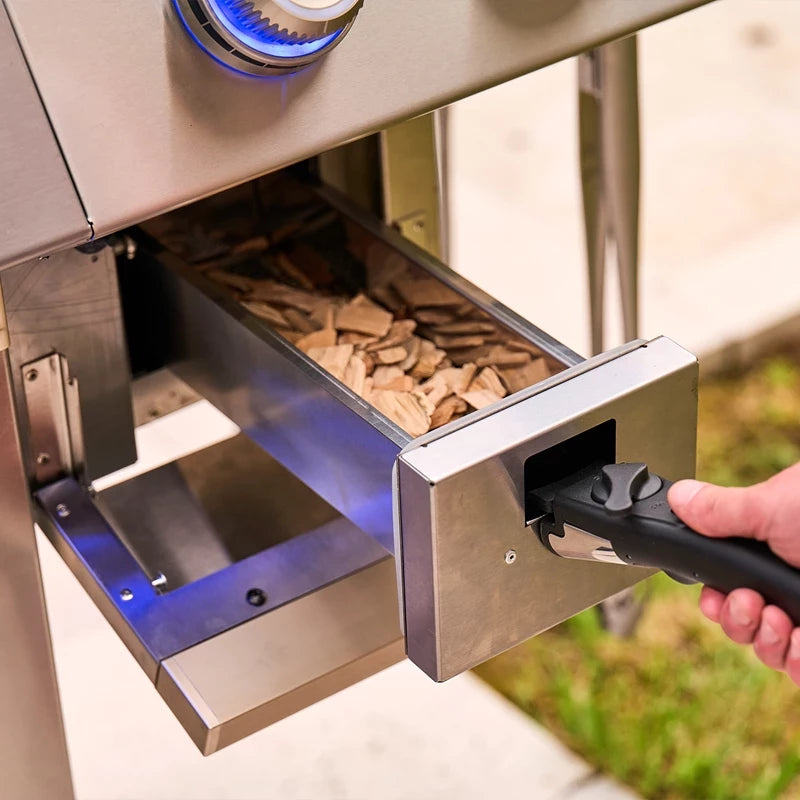 En hånd trekker ut en metallskuff fylt med treflis fra Napoleon Prestige PRO™ 500 Connected, rustfritt stål/svart, og fremhever hvor praktisk og nyskapende denne luksusgrillen er.