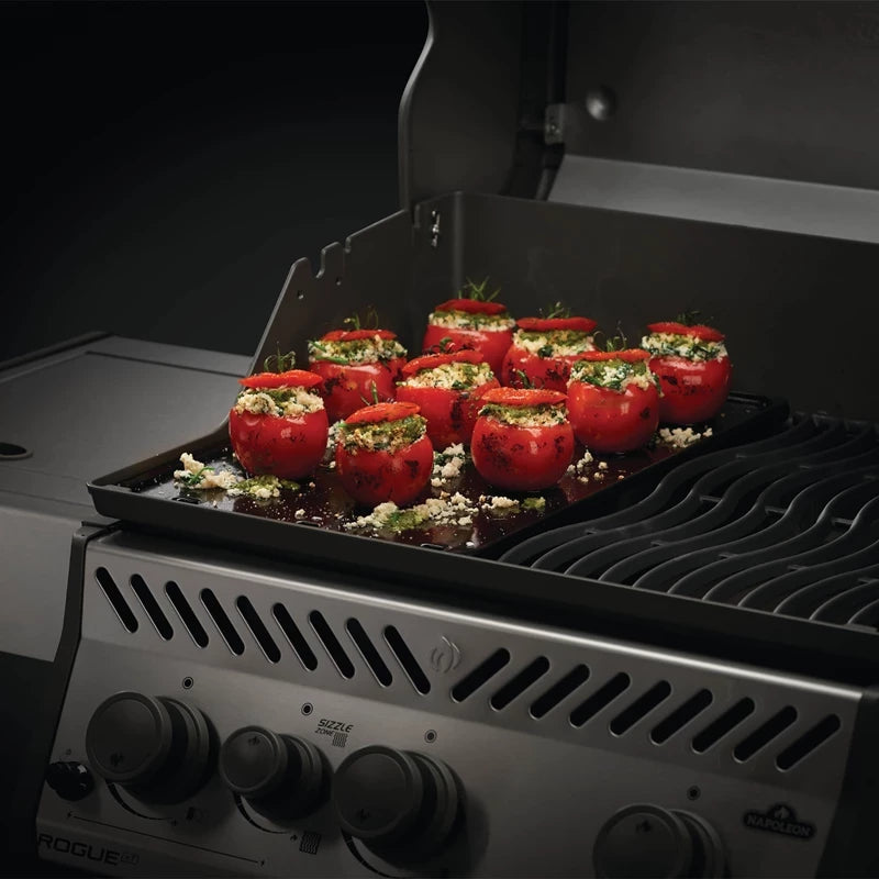 Et brett med fylte tomater med urter og ost står på grillen med lokket åpent, klar til å tilberedes på Napoleon Stekeplate.