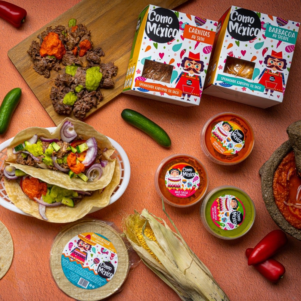 Como Mexico Barbacoa 300 g | Meksikansk Tacokjøtt står på et bord med taco, salsabøtter, paprika, maisskall og Como México-emballasje.