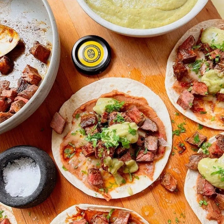 Tre Gran Luchito Soft Taco Wraps (300 g), toppet med terninger av grillet kjøtt, grønn saus og hakkede urter, ligger på en treplate og fanger den livlige essensen av meksikansk gatemat. Like ved står skåler med saus, salt og ekstra kjøtt som fullender dette soft taco-måltidet.
