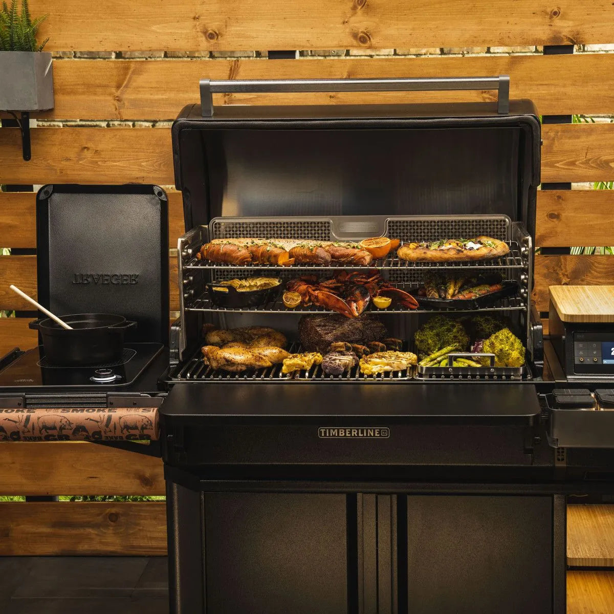 Traeger Timberline XL pelletsgrill er vist utendørs med lokket åpent, og griller kjøtt, grønnsaker og sjømat på flere rister mens en gryte putrer på sidebrenneren - perfekt til utendørs matlaging.