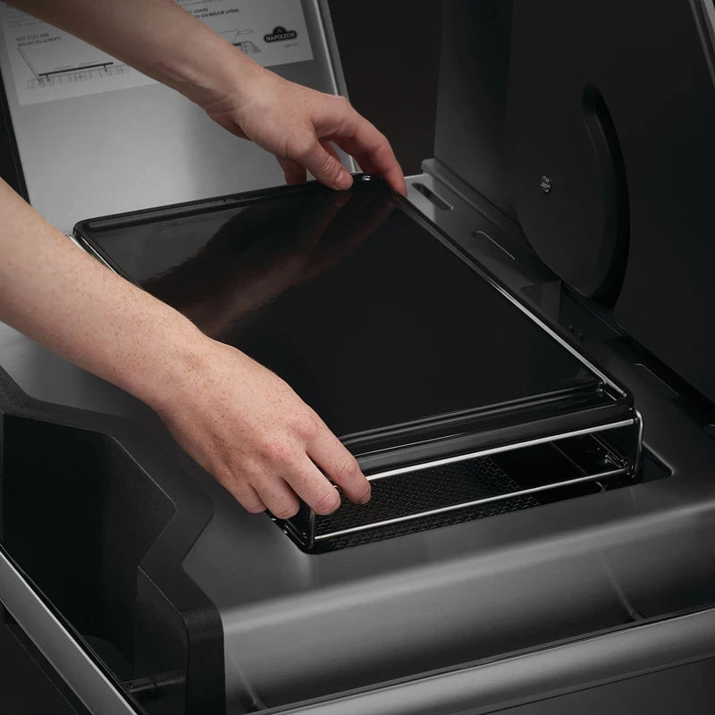 En person setter inn eller tar ut Napoleon Stekeplate til SIZZLE ZONE, stor fra et metallrom inne i en grill eller SIZZLE ZONE-røyker.