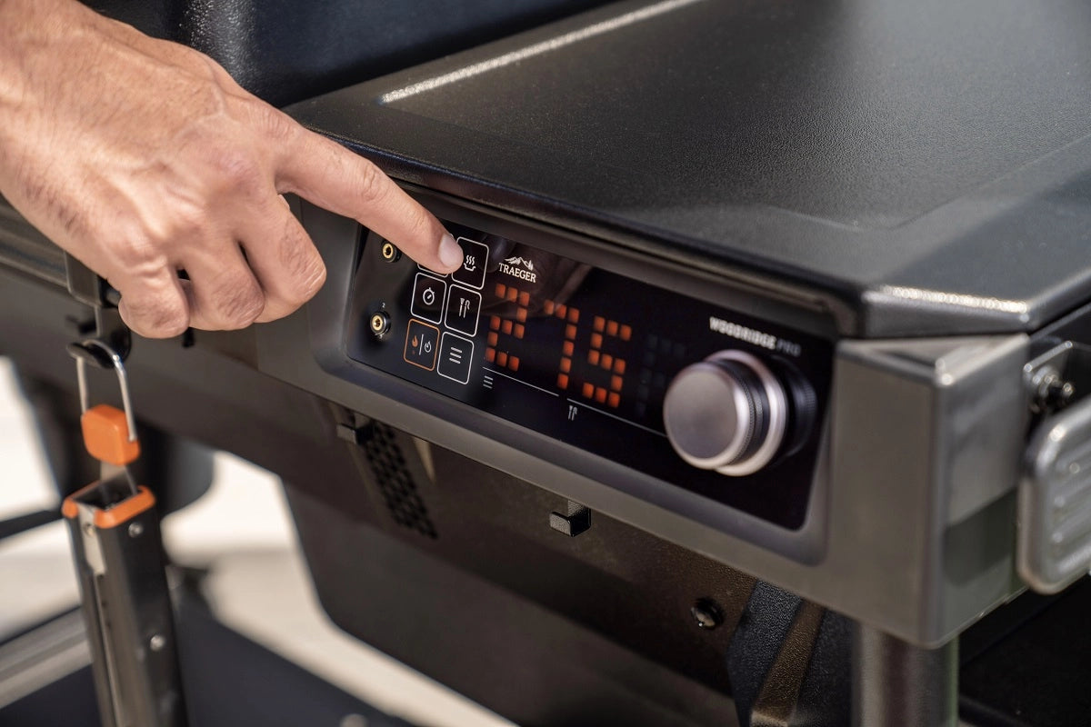 En hånd trykker på en knapp på det digitale kontrollpanelet på den svarte Traeger Woodridge Pro (Forhåndsbestilling) pelletsgrill med WiFIRE-teknologi.