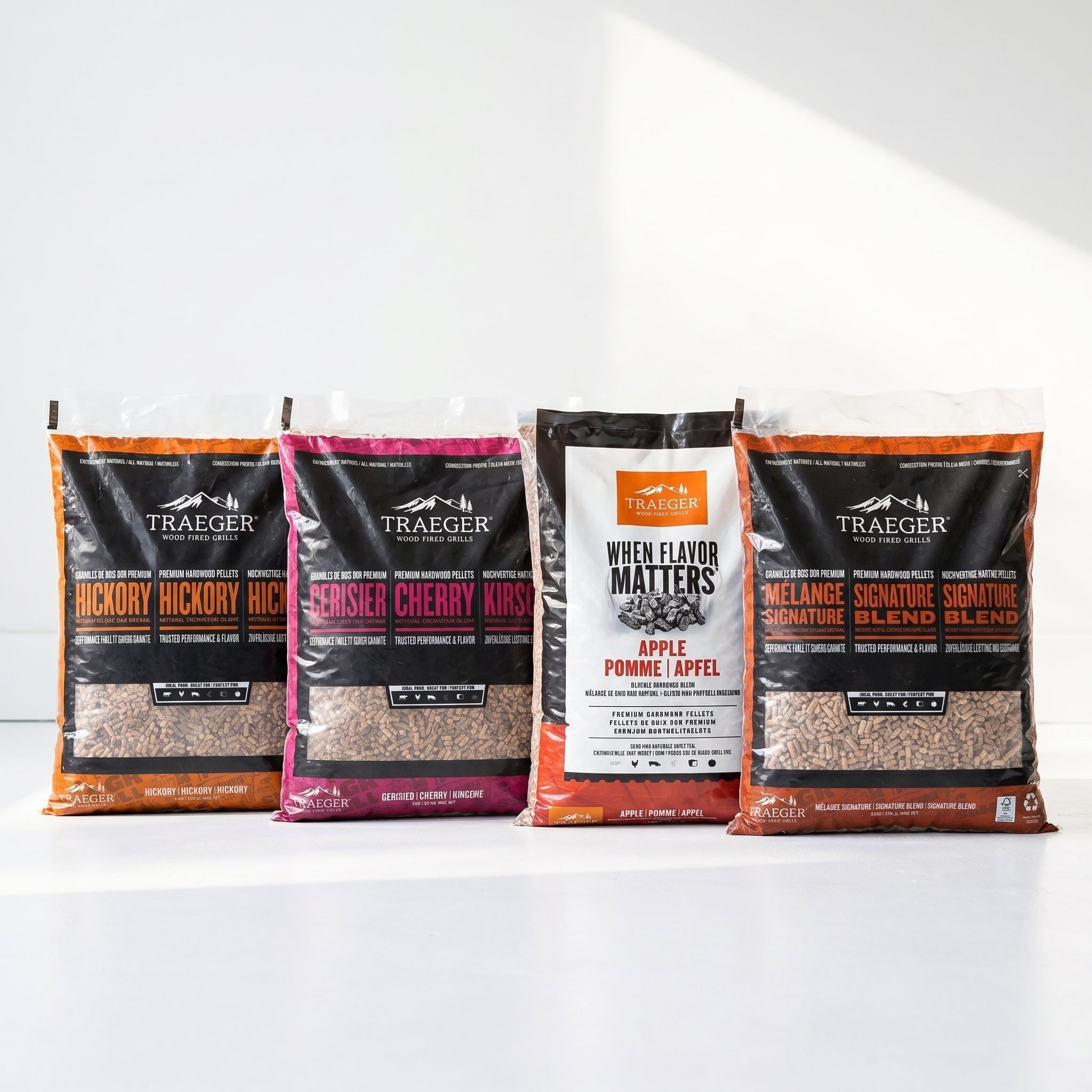 Traeger Pellets Smakspakke 4 varianter-Hickory, Cherry, Apple og Signature Blend-står på en hvit overflate mot hvit bakgrunn, klare til å gi grillmaten din en rik røykaroma.
