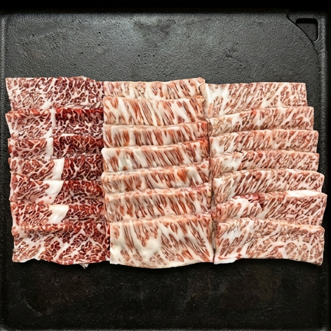 Tynnskårne, vakkert marmorert Storfe Wagyu A5 Yakiniku-biter er pent lagt i rekker på en svart overflate, klare til tilberedning.