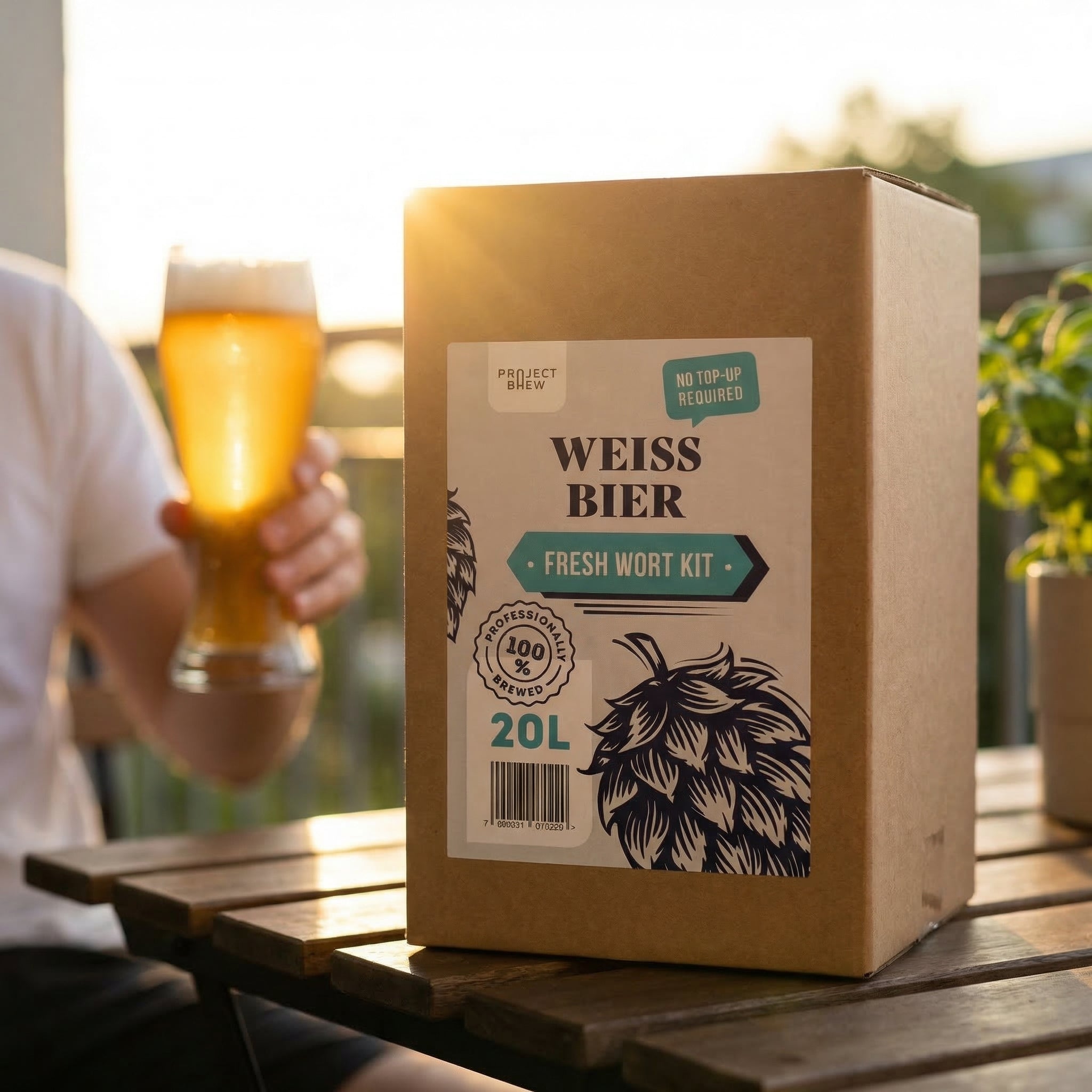 En person holder et glass øl ved siden av en stor eske merket Weissbier - 20L Fresh Wort Kit, ideelt for brygging av ditt eget hveteøl i tysk stil på et bord utendørs.
