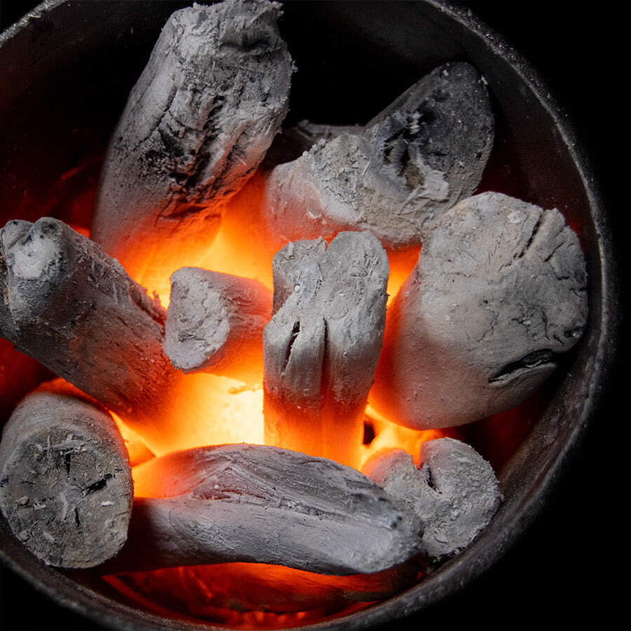 Glødende kull med oransje glør i en metallbeholder - ideelt for opptenning og slukking av kull med YAKINIKU Binchopan, ditt førsteklasses valg for grilling.