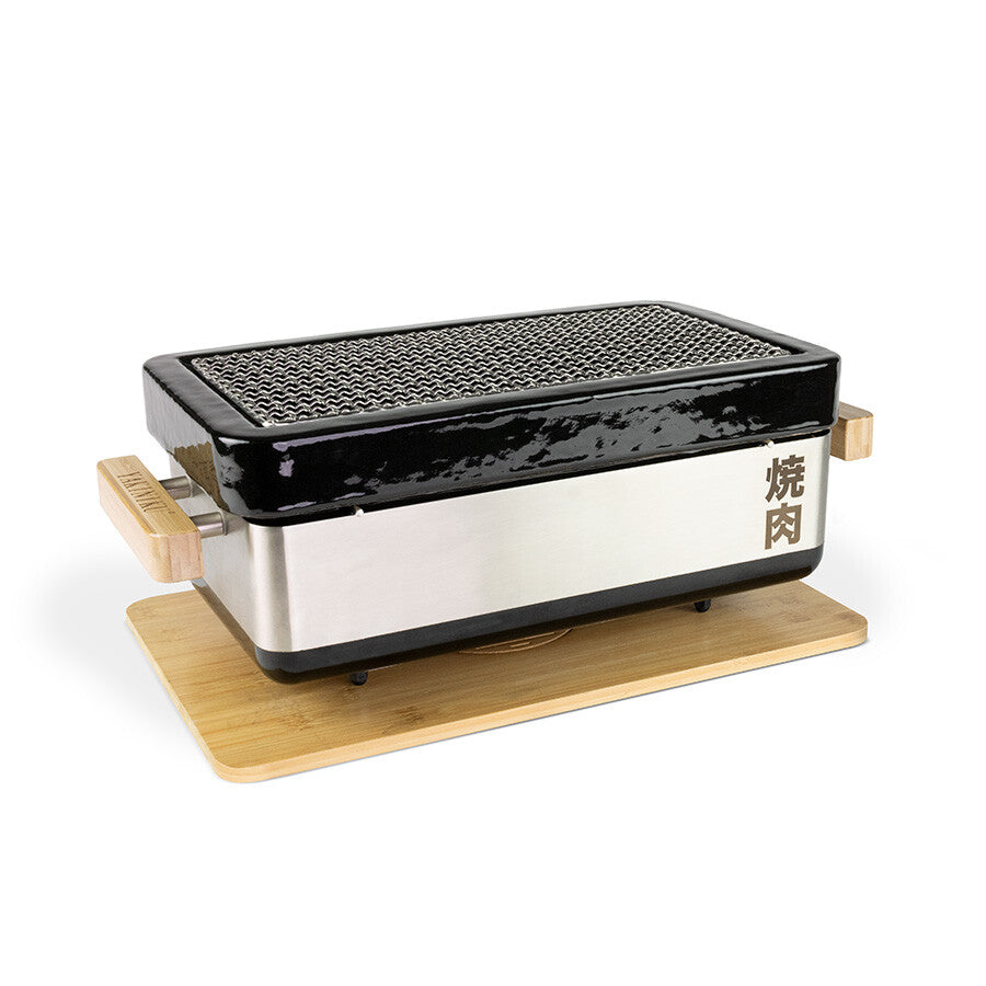 YAKINIKU MEDIUM Rectangular Shichirin PRO er en konro- og yakitori-grill med metallrist, svarte keramiske sider, trehåndtak og japanske tegn på forsiden, plassert på en treplate.