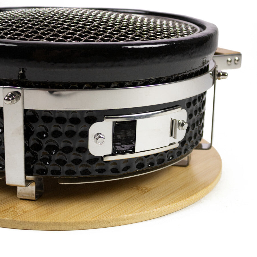 Nærbilde av YAKINIKU Round Shichirin Japansk Bordgrill - en svart keramisk grill med strukturert overflate, metallbeslag og trebunn - ideell for autentisk yakiniku-grilling.