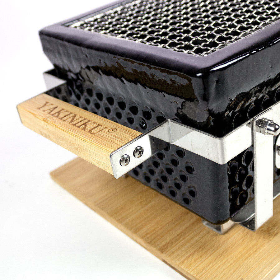 Nærbilde av YAKINIKU Rectangular Shichirin | Konro & Yakitori Grill - svart keramikk med metallrist og trehåndtak, plassert på en trebunn. En elegant japansk bordgrill som er ideell for grilling på bordet.