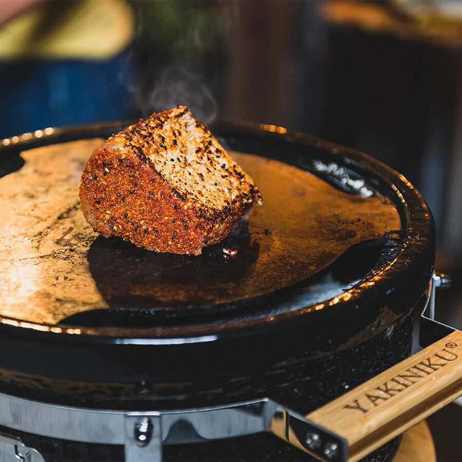 Et krydret kjøttstykke syder på YAKINIKU Shichirin Teppanyaki Plate Rund, Medium, med damp som stiger opp fra den rustfrie ståloverflaten.