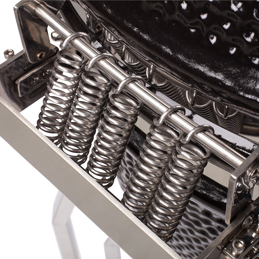 Nærbilde av fire metallfjærer festet til en polert metallramme på YAKINIKU Kamado XLARGE Complete-grillen, med en del av den svarte teksturerte overflaten synlig over.